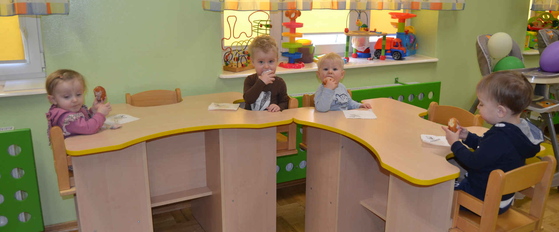 Dzieci siedzą za biurkami i jedzą pączki